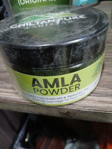 Close-up of a customer's Amla Powder, sealed in a black jar with a green label on a shelf.