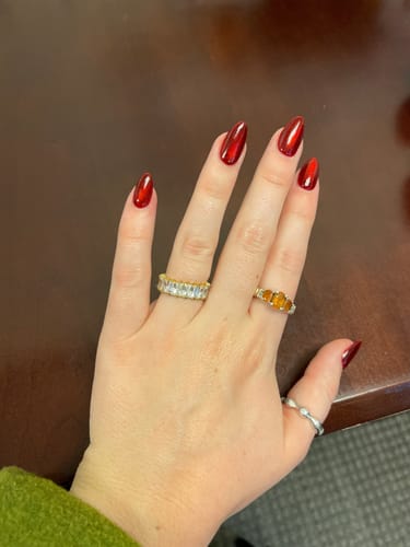 Reviewer's hand wearing the gold Asriel Ring with three amber-colored stones on the middle finger, shown with other rings.