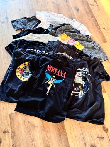Customer's pile of assorted Rock & Music T-Shirts, including Nirvana and Guns N' Roses, spread out on a floor.