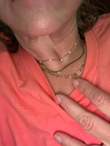Close-up of a reviewer wearing the Chelsea Herringbone Necklace layered with two other gold necklaces.
