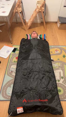 Anmelder ligger i det sorte infrarøde saunatæppe på et gulv derhjemme.