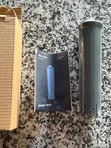 Reviewer's new replacement water filter with its instruction booklet and box, displayed on a granite countertop.