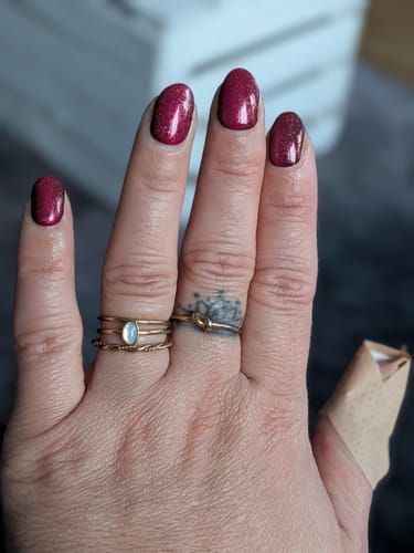 Kundin zeigt ihre manikürten Nägel mit den glitzernden, bordeauxroten UV-Gel-Folien 'Taunted'.