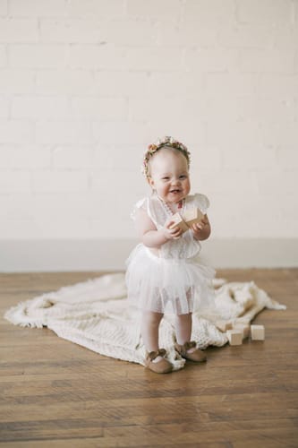 Customer's baby smiling while wearing a delicate white romper with a tulle skirt.
