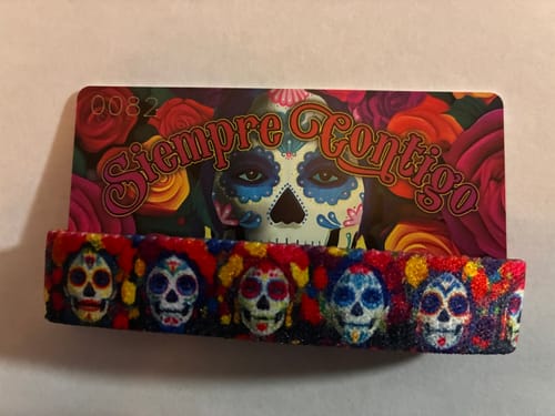 Reviewer's Siempre Contigo Bracelet with a colorful sugar skull pattern, shown with its matching collector's card.