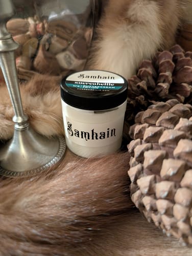 Customer's Samhain Buttercream Lotion jar displayed on rustic fur next to a large pinecone.