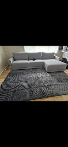 Customer's textured charcoal Relax Mat in a living room, placed on a wooden floor in front of a grey sofa.