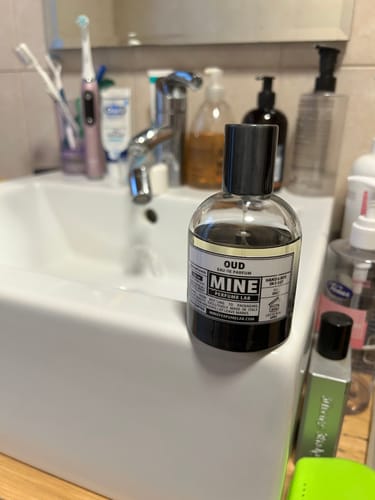 Recensore mostra il suo profumo OUD appoggiato sul bordo di un lavandino bianco in bagno.