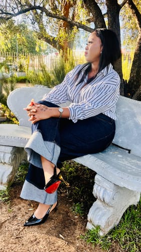 Customer wearing the shiny black pointed-toe high heel sandals, showing the red sole while sitting on a bench.