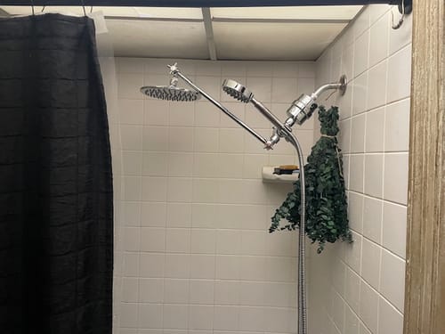 Customer's new Adjustable Shower Arm installed in a white tiled shower with a rain head and handheld sprayer.