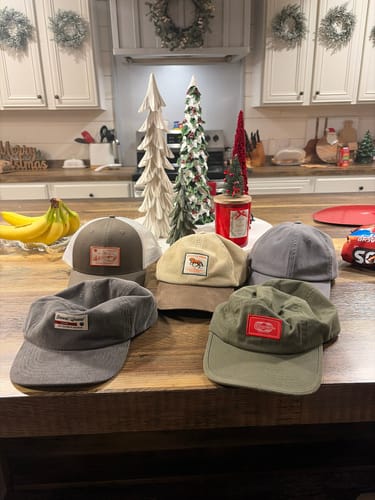 Reviewer's collection of five Big Trucker Hats in various colors and styles displayed on a wooden kitchen table.