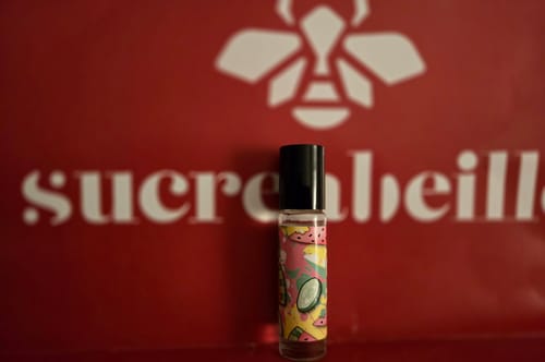 Customer's Cucumber Melon Bitch rollerball with a colorful label, pictured in front of a red background with the brand's logo.