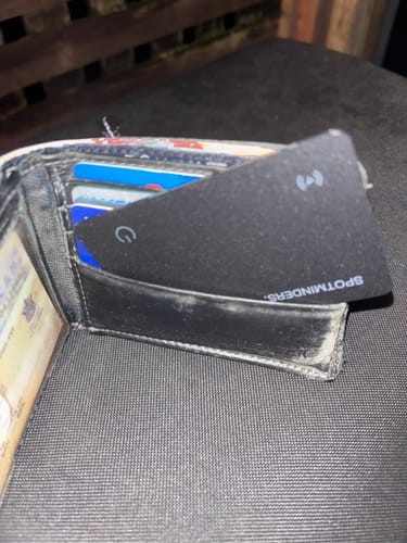 Customer's black SPOTMINDERS Tracking Card shown inside an open, worn wallet on a textured surface.