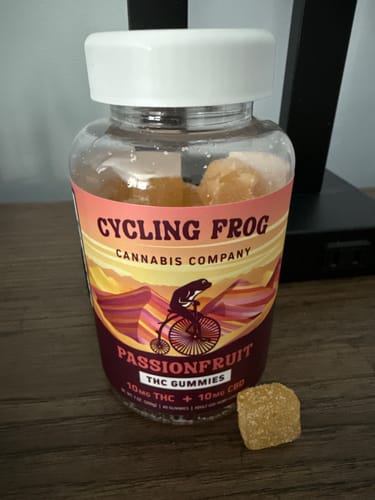 Customer's jar of Cycling Frog Passionfruit Gummies on a table with one sugar-coated gummy beside it.