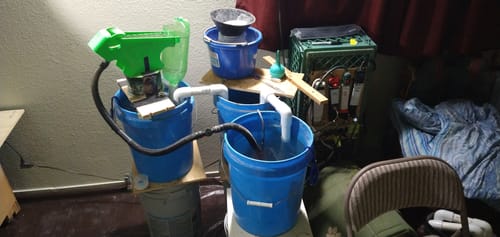 Reviewer's Buddy Sluice Mat set up in a custom indoor recirculating system with buckets and hoses for gold prospecting.