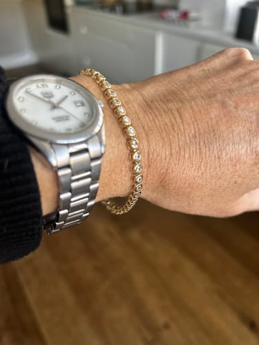Customer wearing the gold Classic Bezel Tennis Bracelet on their wrist next to a watch.