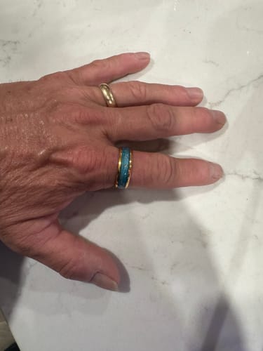 Customer's hand wearing the Orelian ring on the middle finger, showing its turquoise inlay and gold band against a marble surface.