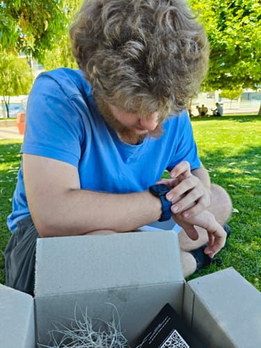 Customer sits on the grass looking at their new Gard Pro Health Smartwatch 2 on their wrist.
