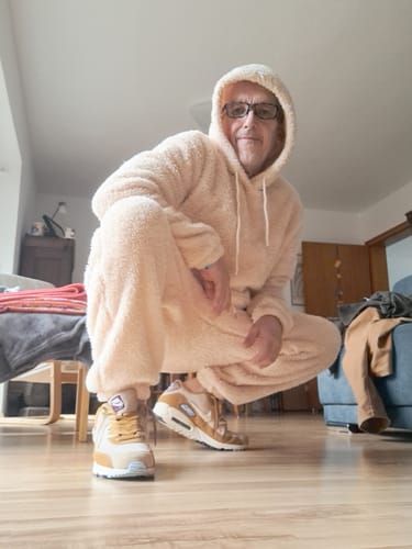 Reviewer squatting in a living room while wearing the fluffy teddy hoodie and jogger pants set with the hood up.