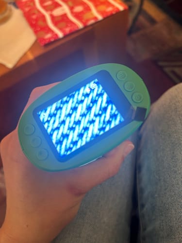 Ein Kunde hält das grüne Edubini Abenteuer-Mikroskop, dessen Bildschirm eine vergrößerte, blau leuchtende Struktur zeigt.