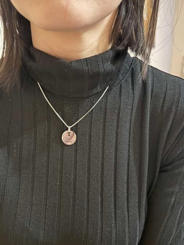Customer wearing the Stellar Names necklace with a silver-colored chain and round pendant over a black turtleneck.