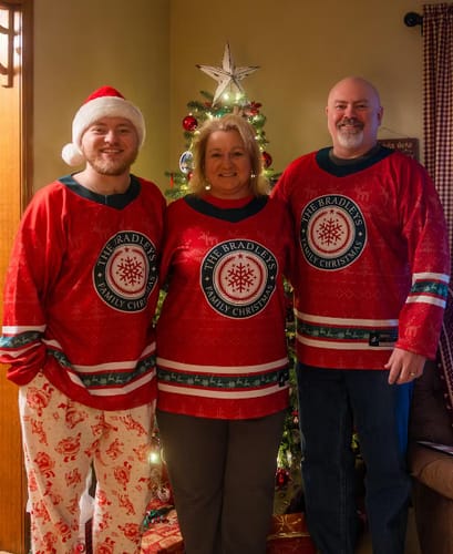 A customer's family of three wearing matching red Family Christmas Custom Hockey Jerseys in front of a Christmas tree.