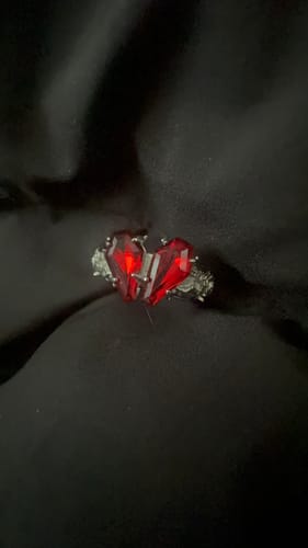 Customer's Promise Ring with two red, coffin-shaped stones forming a heart on an ornate silver band, resting on black fabric.