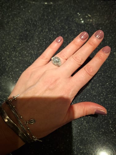 Customer's hand wearing the large, antique style diamond ring on their finger against a dark countertop.