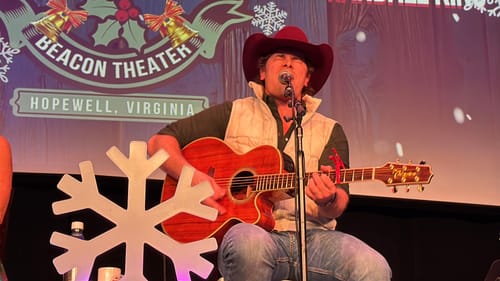 Reviewer's photo of a person playing an acoustic guitar on a decorated stage.