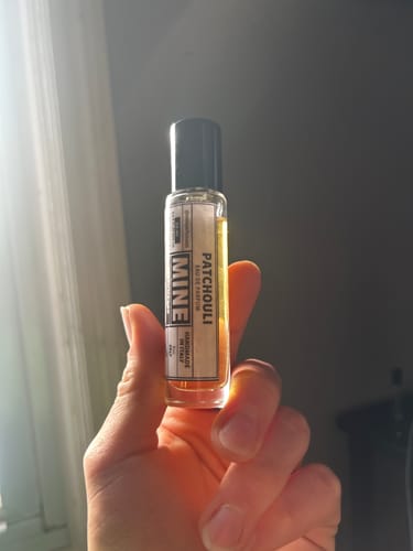 Recensore tiene in mano la boccetta di vetro del profumo PATCHOULI.