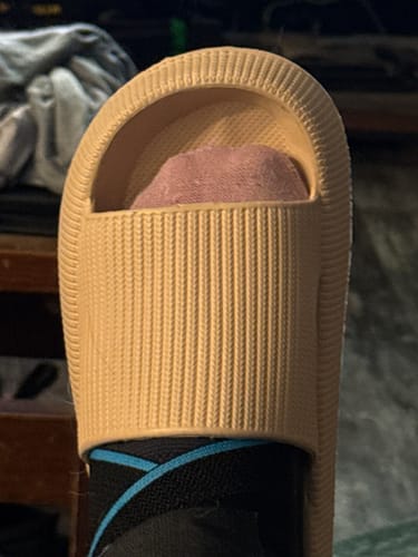 Close-up of a customer's foot in a beige Cloudies slide, worn over a black sock.