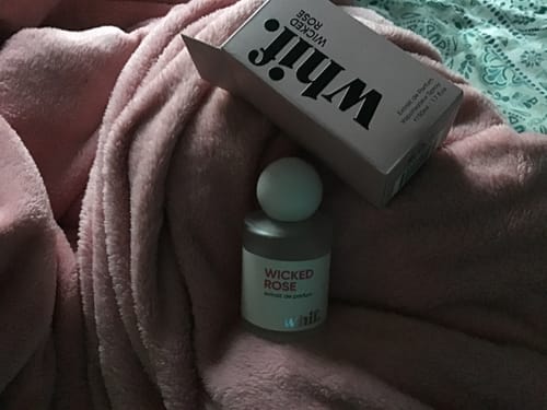 Reviewer's Wicked Rose perfume bottle and box resting on a soft pink blanket.