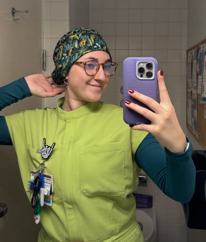 Reviewer in scrubs taking a selfie while wearing the patterned DuoStyle Scrub Hat in a slouchy style.