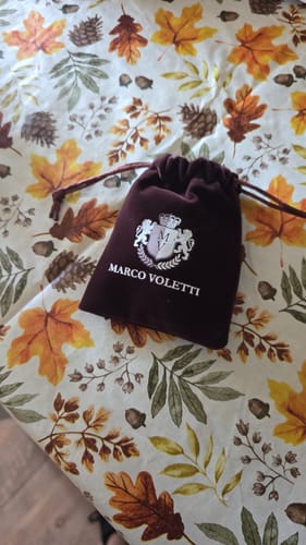 Packaging for the Bravado ring, showing the burgundy velvet pouch with a logo on a patterned tablecloth.