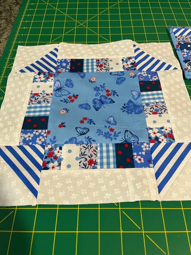 Customer's completed blue quilt block from the Mrs Quilty Subscription Box on a green cutting mat.