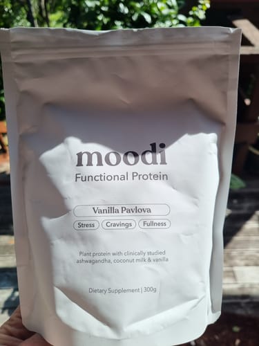 Customer holding a white pouch of moodi Functional Protein in Vanilla Pavlova flavor.