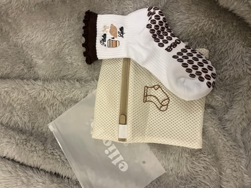Customer's Elliosa Wash Bag with a pair of white grip socks resting on top of a fluffy surface.