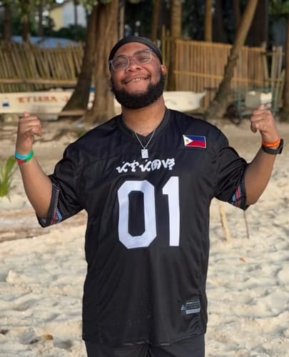 Customer smiling on a beach, wearing the black Philippines Heritage Custom Football Jersey with the number 01.