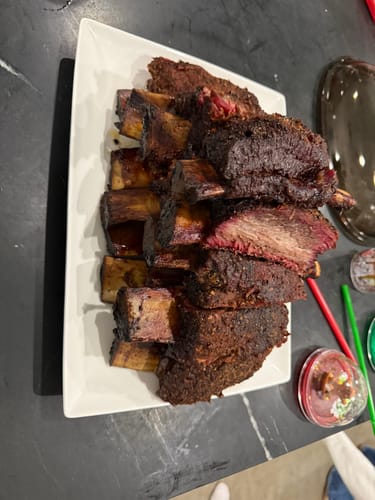 Reviewer's smoked Bone-In Short Ribs with a dark bark, piled high on a white platter.