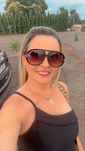 Cliente sorrindo e usando os Óculos Veneza, que possuem uma armação preta e grande com lentes em degradê.