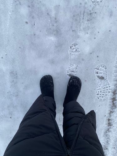 Asiakkaan mustat Vaistoa Sulo -paljasjalkanilkkurit lumisella tiellä, jossa näkyy kengänjälkiä.