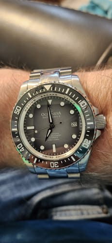 A reviewer's Oceaneva Deep Marine Explorer II watch on their wrist, showing its gray fade dial and stainless steel bracelet.