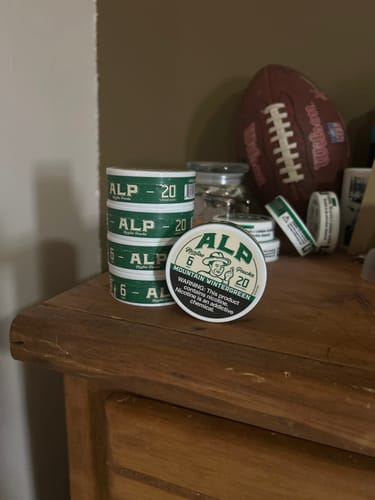 Customer's stacked tins of Mountain Wintergreen Nicotine Pouches on a wooden dresser.