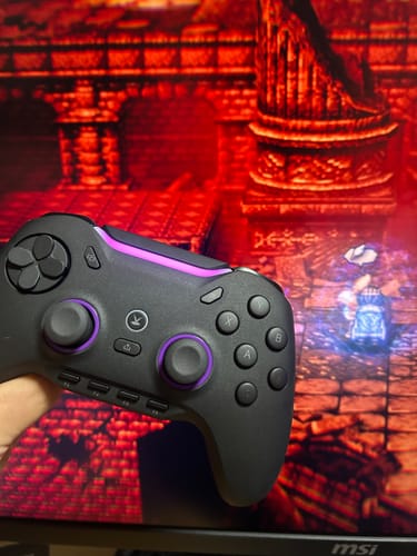 レビューアーが黒と紫のVoid GENESISコントローラーを手に持っています。背景はゲーム画面です。