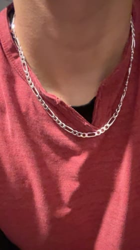 Customer wearing the Heavy Solid Silver Figaro Chain around their neck against a red shirt.