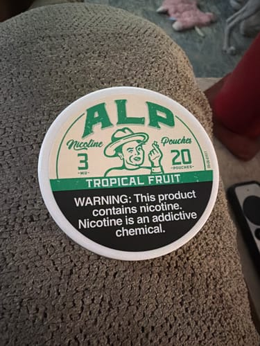 Customer's can of ALP Tropical Fruit 3mg Nicotine Pouches resting on a textured fabric surface.