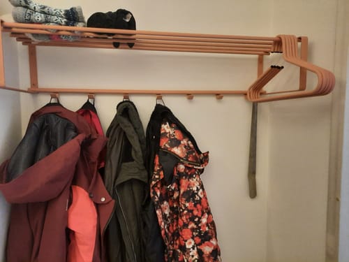 Recensent toont de Spinder Design kapstok Rex 2 XL in Clay Terra, met jassen aan de haken en bijpassende hangers aan de roede.