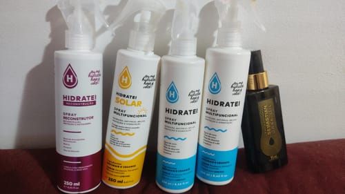 Cliente mostra sua coleção de produtos Hidratei, incluindo os sprays reconstrutor, solar e multifuncional.