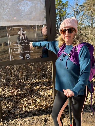 Reviewer standing by a trail sign while hiking in the Ainsley Sweater in Majolica Blue.