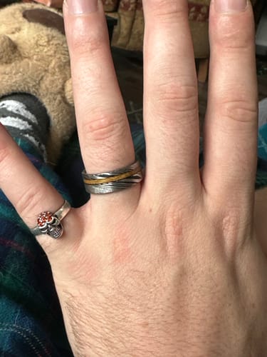 Customer's hand wearing The Harper ring, showing its patterned Damascus steel and central wood inlay.